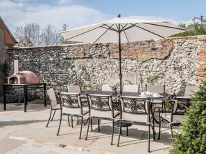 An outdoor patio with a stone wall, a pizza oven, and a table with chairs. - This stunning property is a real treat for history lovers. (Syderstone, near Fakenham)
