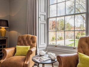 A room with a large window, a brown leather armchair, a small table with a magazine, and a lamp. - This stunning property is a real treat for history lovers. (Syderstone, near Fakenham)