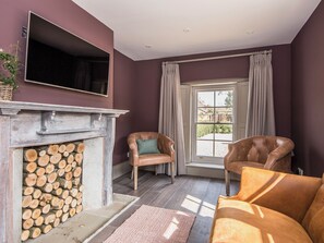 A room with a fireplace, two leather armchairs, a television, and a large window with curtains.