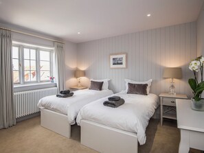 A hotel room with two beds, a window with curtains, a radiator, and a framed picture on the wall.