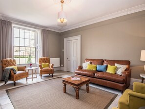 A living room with a brown leather sofa, two armchairs, a coffee table, and a radiator.
