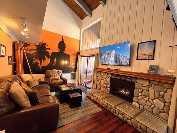 Amplia sala de estar con un sofá grande, una chimenea de piedra, un televisor y un mural de Buda.