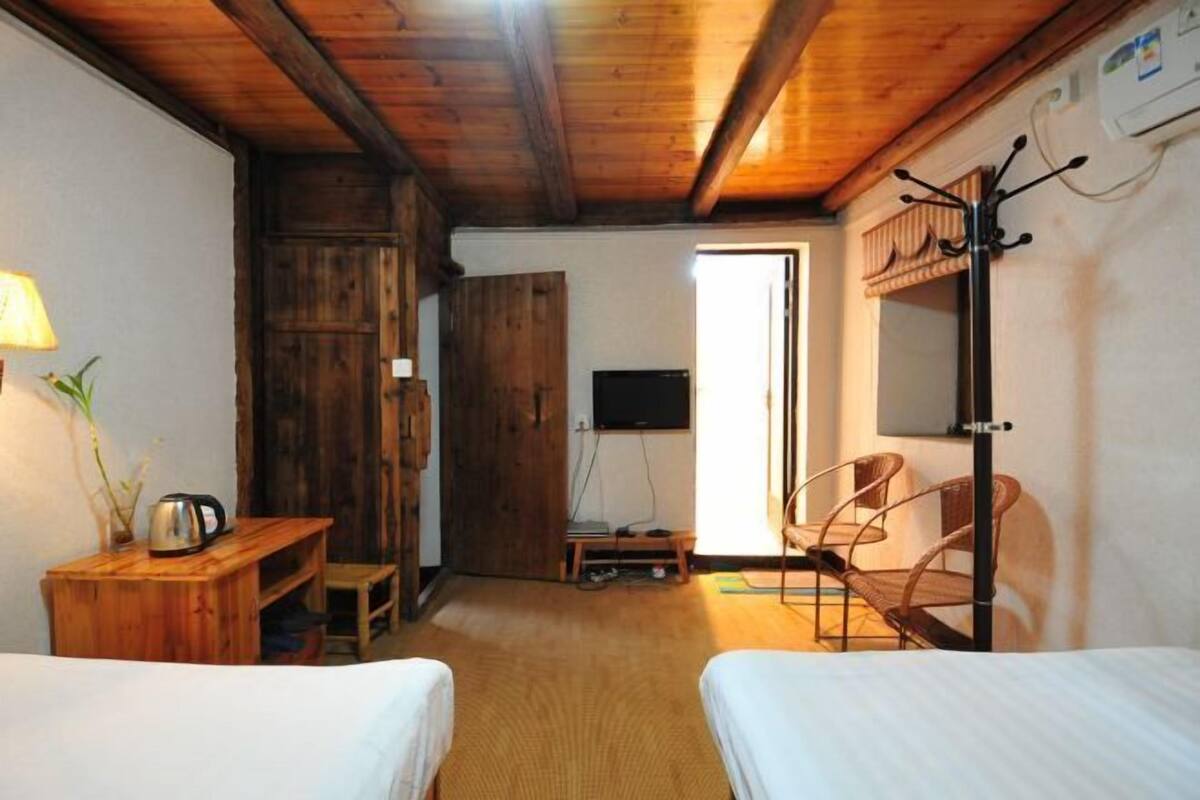 A room with two beds, a wooden desk, a chair, a television, and a coat rack.