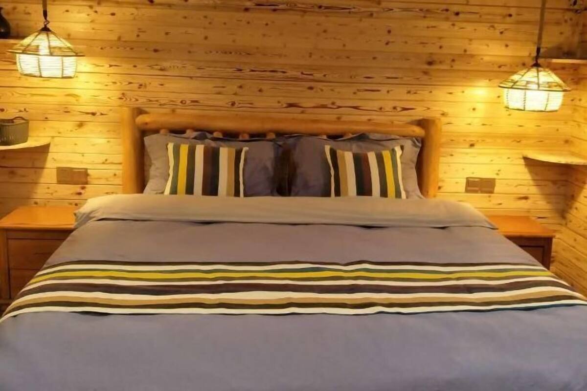 A wooden cabin-style bedroom with a bed, striped bedding, and two hanging lamps.