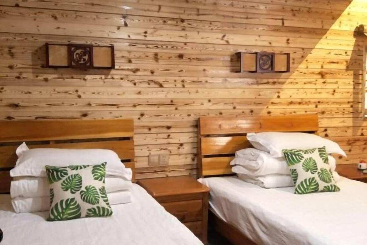 A wooden-paneled room with two beds, each with white bedding and green leaf-patterned pillows.