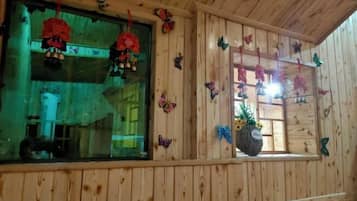 A wooden cabin interior with multiple windows, some adorned with hanging decorations.