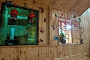 Interior de una cabaña de madera con varias ventanas, algunas decoradas con adornos colgantes.