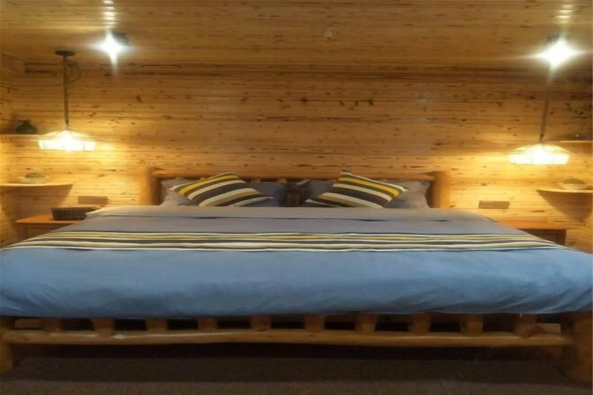 A wooden cabin-style bedroom with a bed, pillows, and bedside lamps.