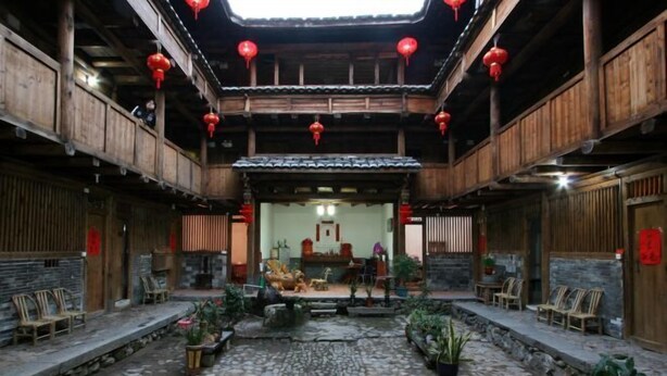 Un bâtiment traditionnel en bois, doté d’une cour en pierre, de lanternes rouges et de meubles en bois.