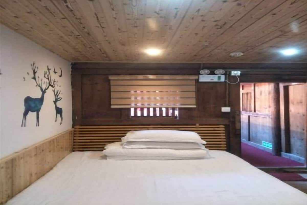 A wooden room with a bed, a wall mural of deer, and a window with blinds.