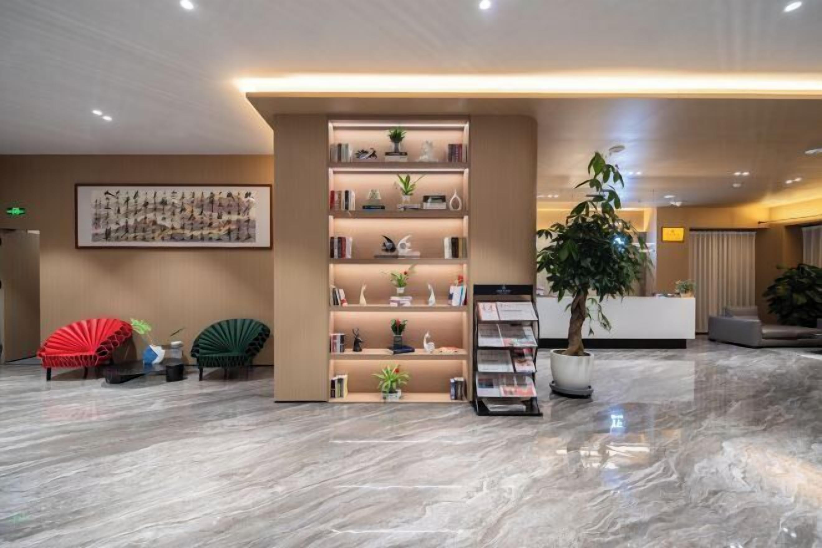 A modern lobby with a marble floor, a reception desk, a bookshelf, and two chairs.
