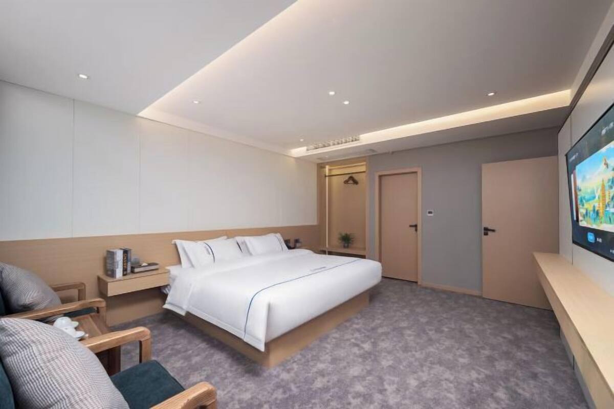 A modern hotel room with a large bed, a desk, a chair, a TV, and a door.