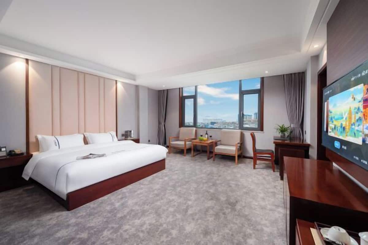 A hotel room with a large bed, a seating area with a table, a TV, and a city view.
