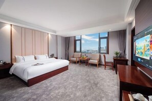 A hotel room with a large bed, a seating area with a table, a TV, and a city view. - Mengzi Yufeng Hotel (Mengzi)