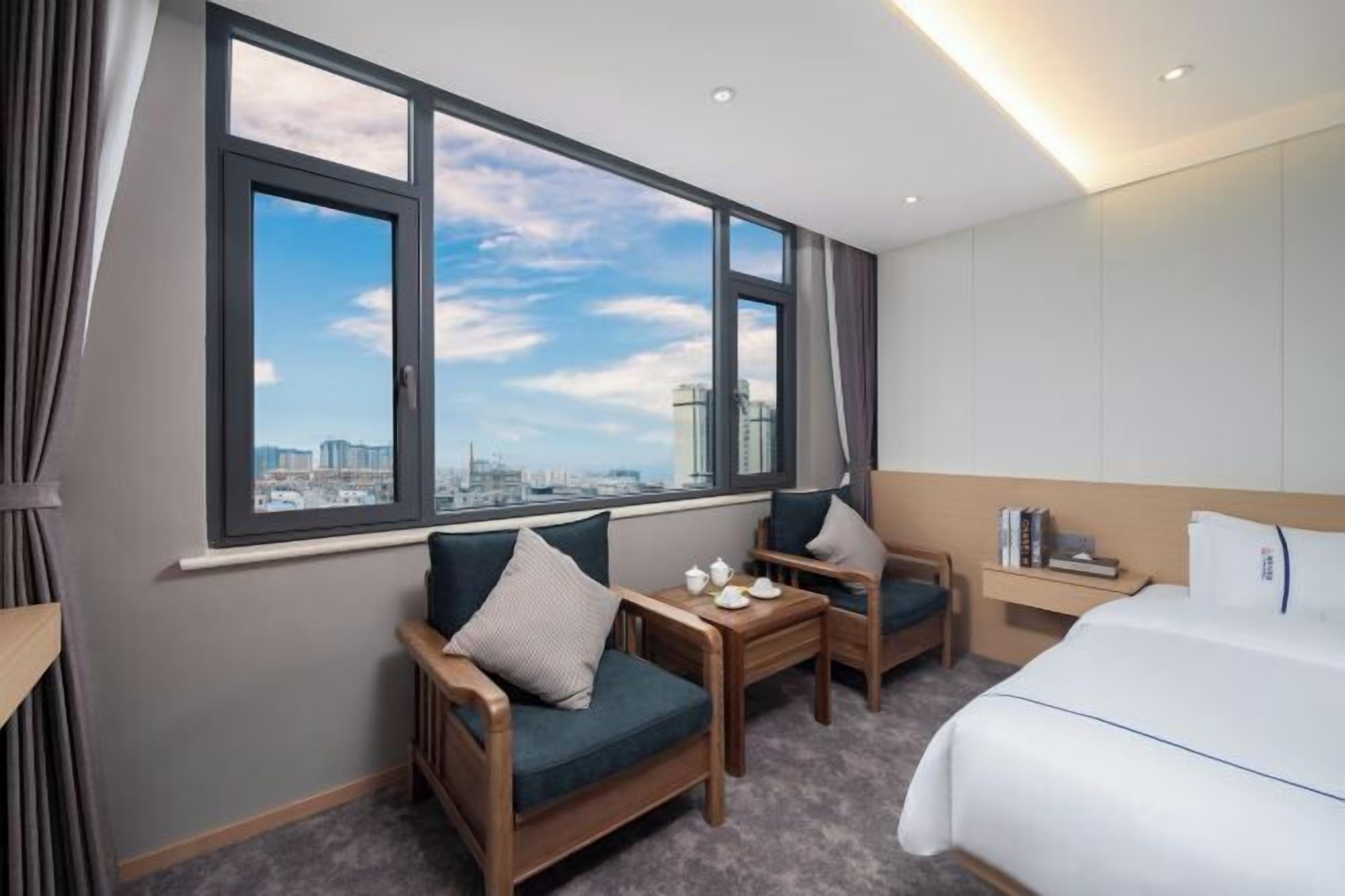 A hotel room with a large window, a bed, a small table, and a chair.