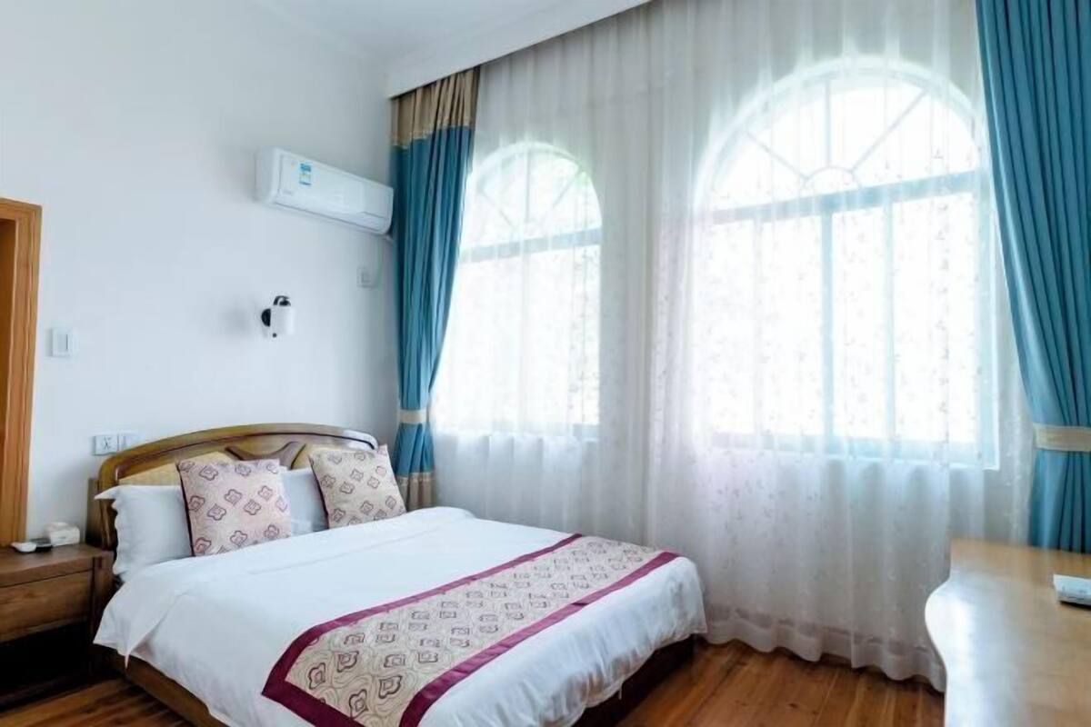 Habitación de hotel con una cama de madera, una mesita de noche, un equipo de aire acondicionado y una ventana con cortinas.