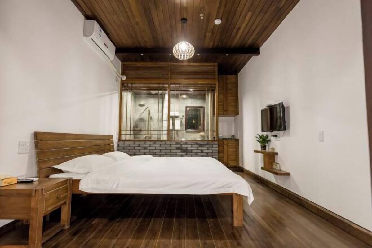 Un dormitorio con una cama de madera, una mesita de noche, un televisor y una ventana con vistas al exterior.