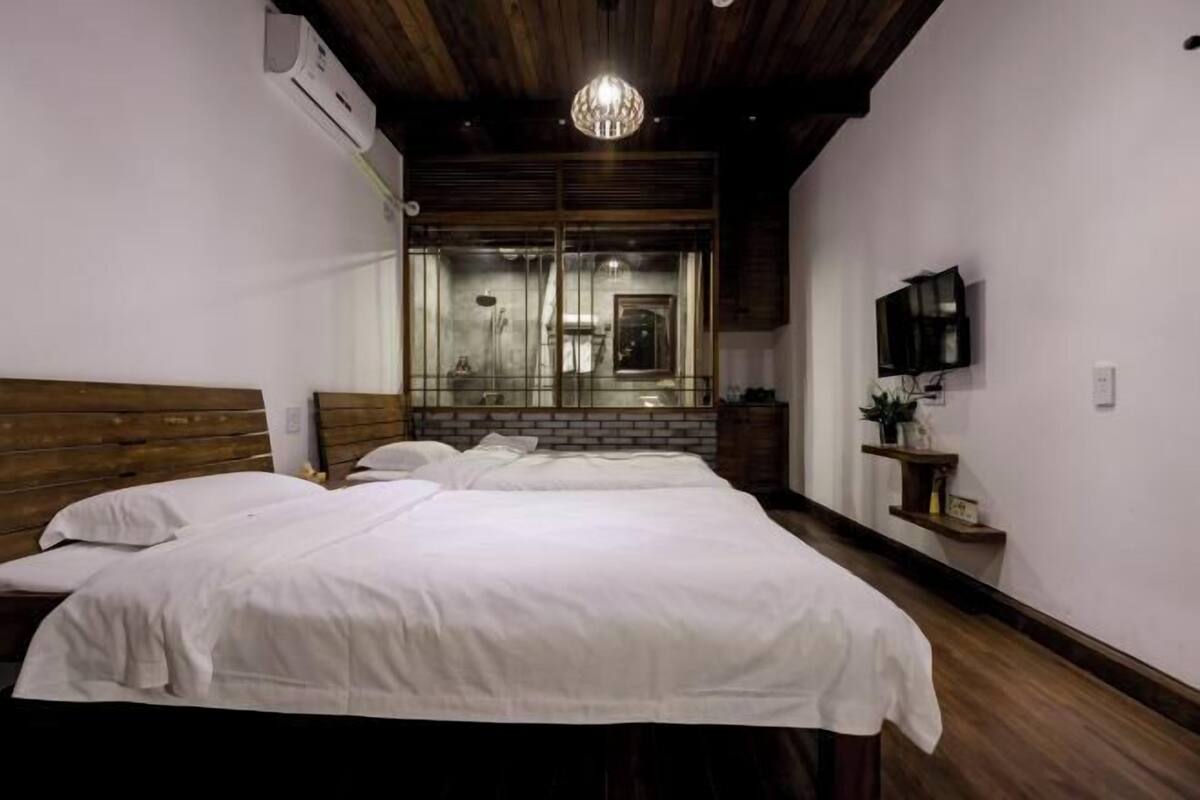 Un dormitorio con dos camas, techo de madera, candelabro, televisor y un espejo que refleja la habitación.