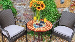 A wicker table with a mosaic top, two wicker chairs, a vase with sunflowers, a bottle of champagne, and a glass of orange juice.