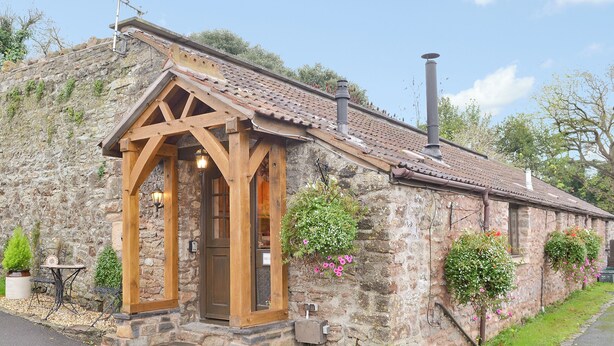 A stone building with a wooden entrance, a chimney, and potted plants.