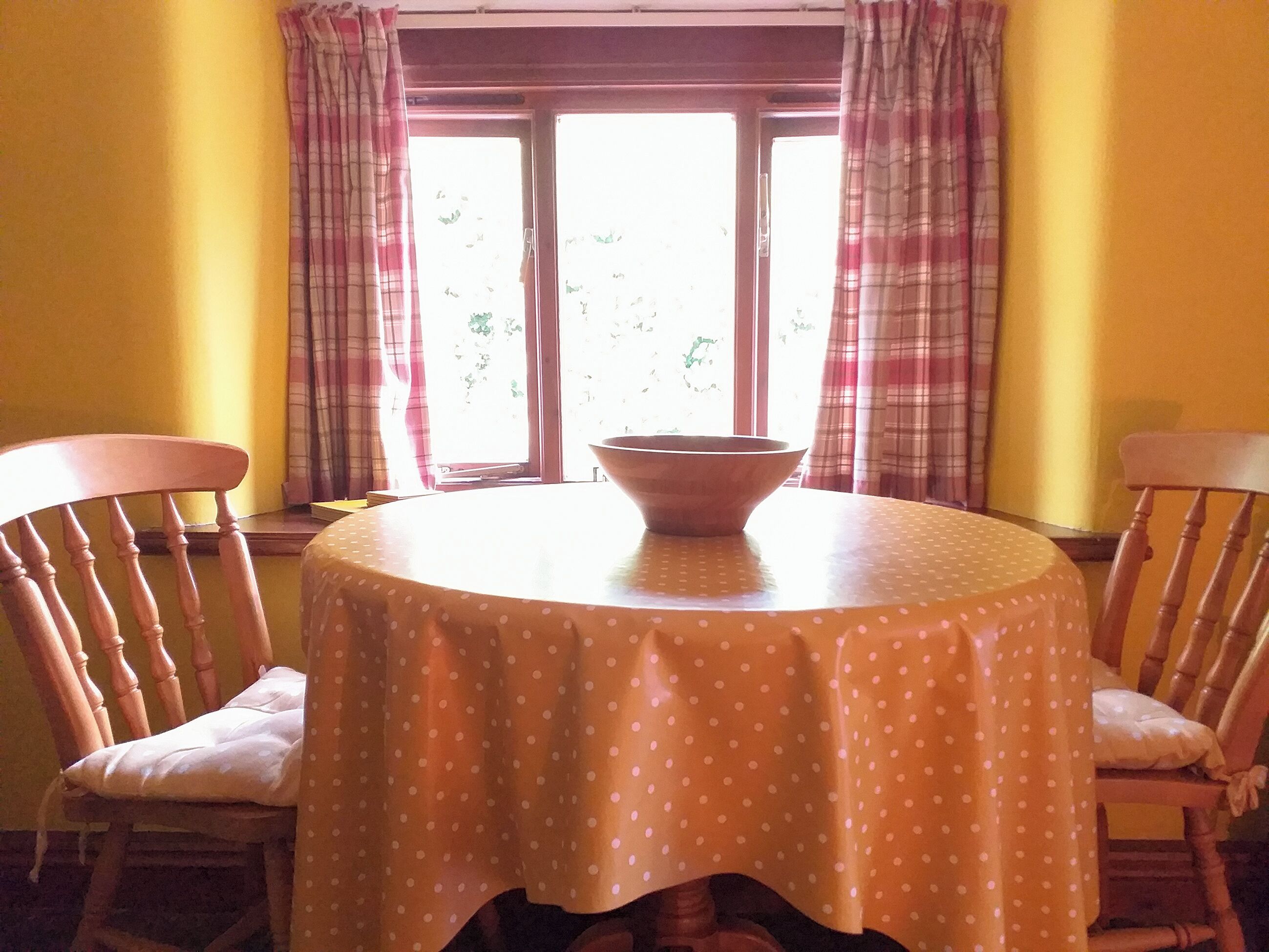 A dining table with a polka dot tablecloth, two wooden chairs, and a bowl on the table.