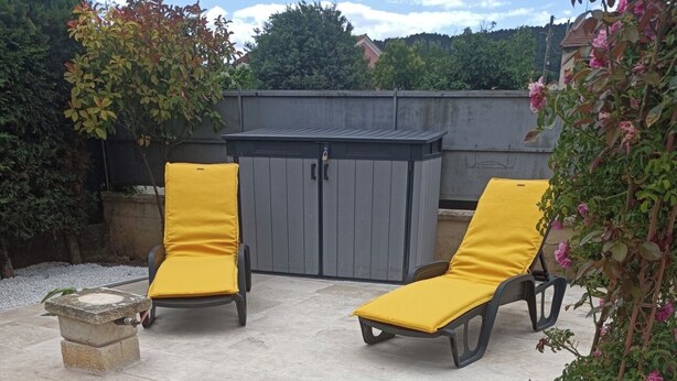 A poolside area with two yellow lounge chairs, a stone planter, and a grey fence in the background.