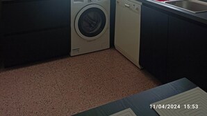 A compact kitchen with a washing machine, a sink, and a window with curtains.