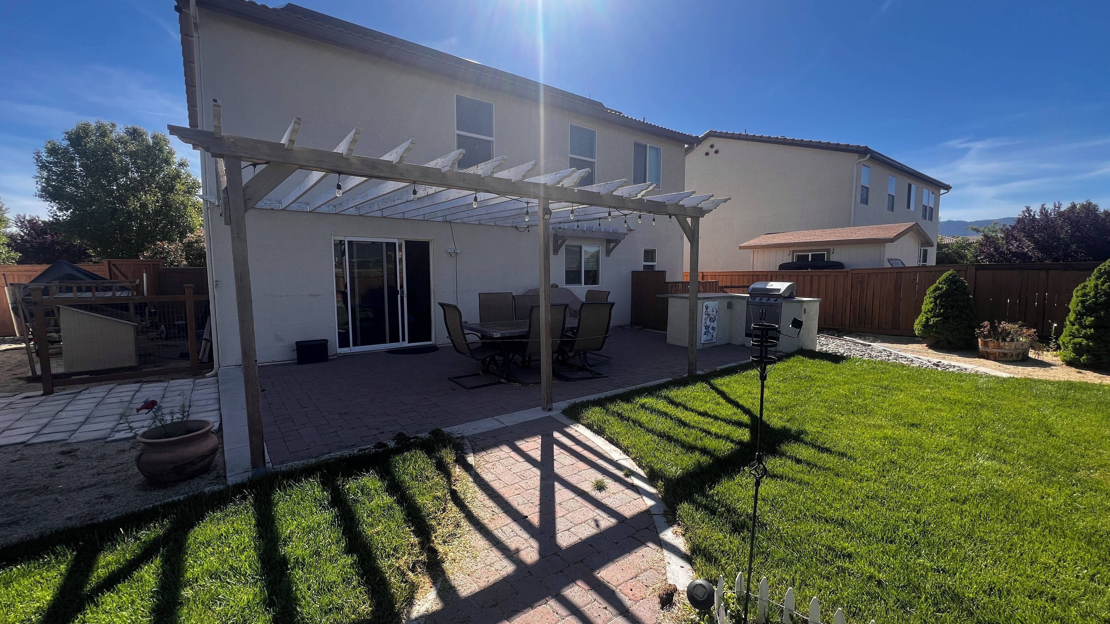 A backyard with a covered patio, a barbecue grill, and a fenced play area.