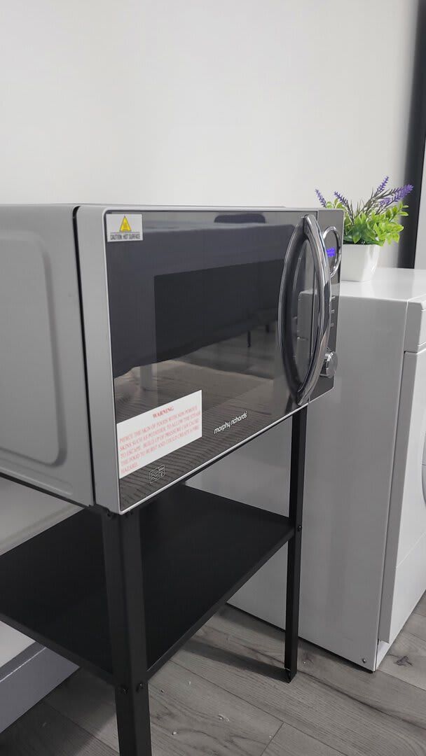 A compact, modern washing machine with a transparent door, placed on a black metal stand.
