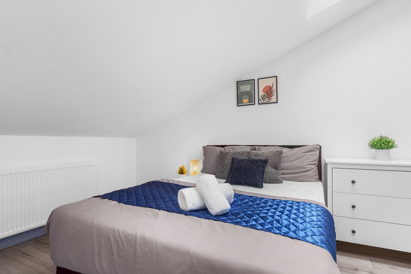 A bedroom with a bed, bedside table, lamp, and a small potted plant.