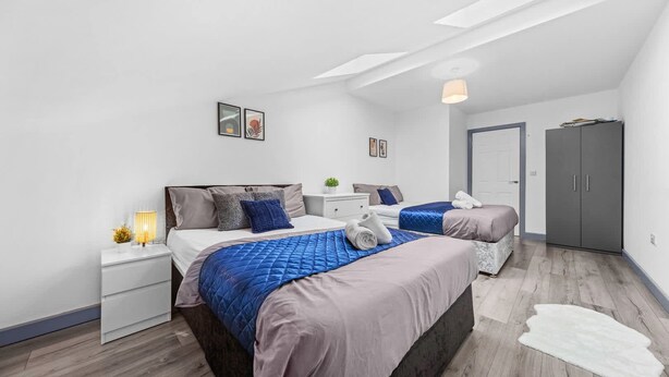 Une chambre moderne avec deux lits, une table de chevet avec une lampe, une armoire et une porte.