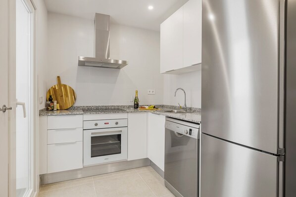 Una cocina moderna con armarios blancos, una campana de acero inoxidable, horno integrado, lavavajillas y un refrigerador grande.
