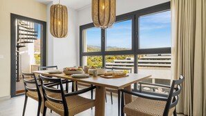 A dining area with a wooden table, woven chairs, and large windows offering a view of the cityscape. - Casa Carmen - Rooftop Luxury Penthouse Estepona (Estepona)
