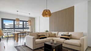 A modern living room with a sectional sofa, a coffee table, and a dining area with a view of the cityscape. - Casa Carmen - Rooftop Luxury Penthouse Estepona (Estepona)