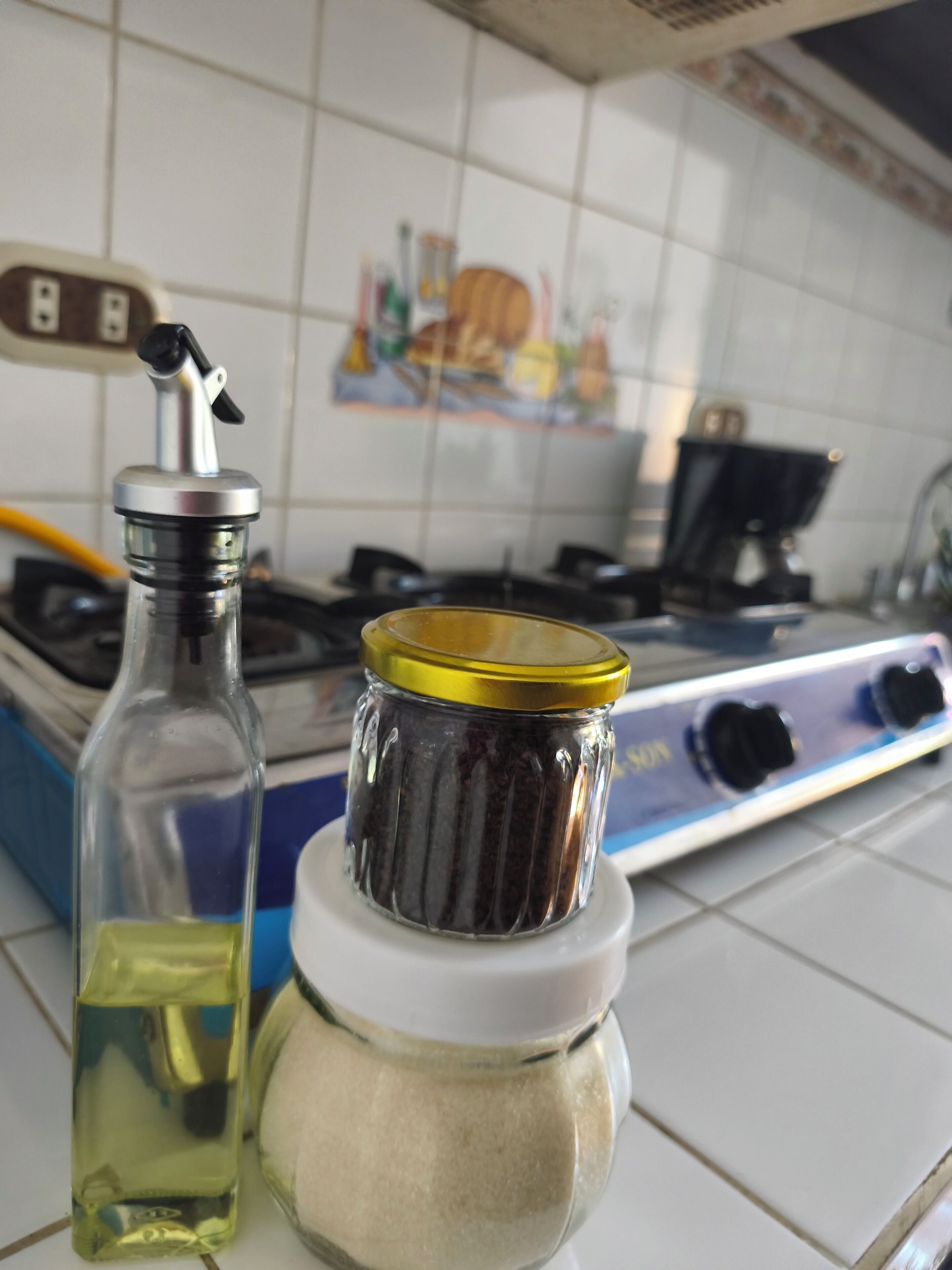 Een keuken met een gasfornuis, een fles olie en een kruidenpot.