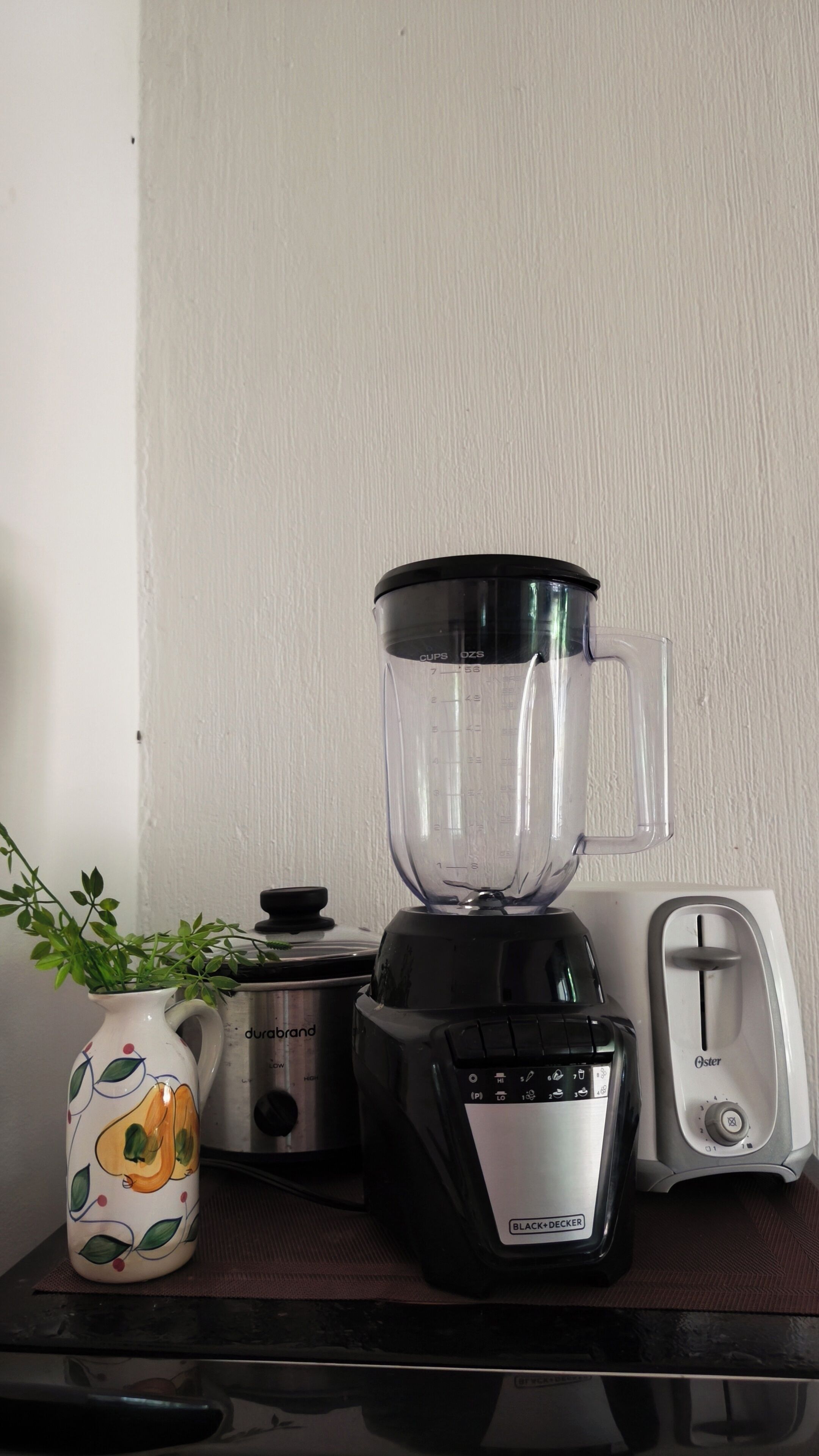 Un piano di lavoro in cucina con un frullatore, una macchina per il caffè e un vaso decorativo.