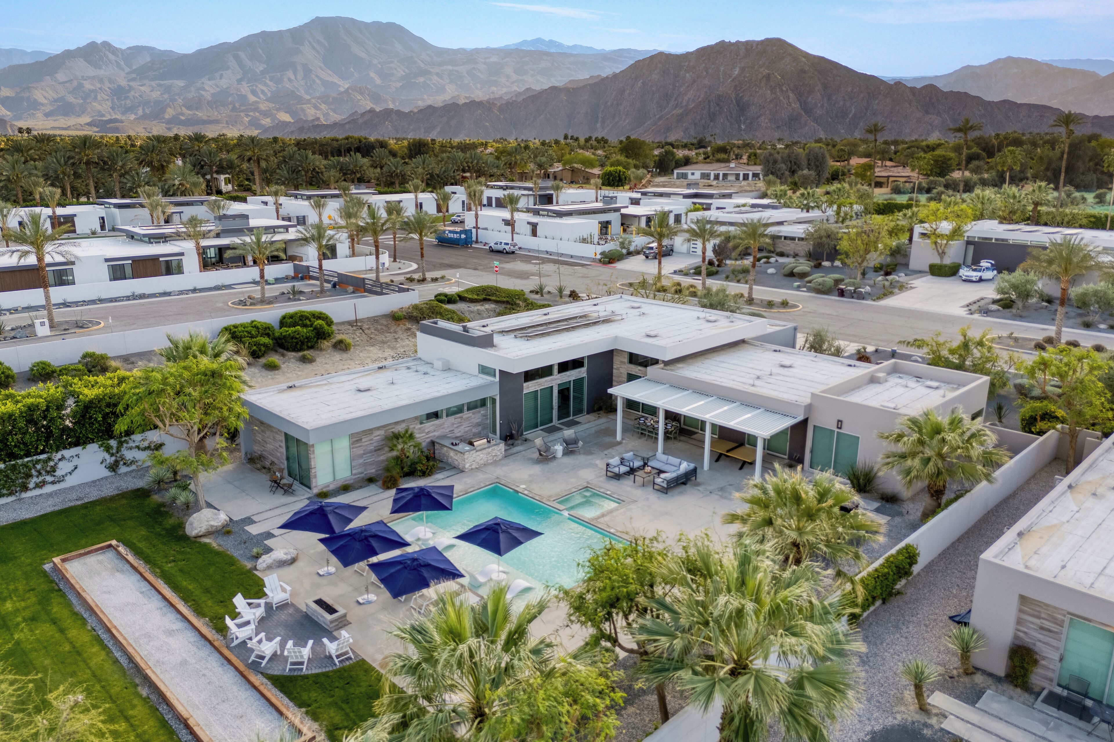 A modern resort with multiple buildings, a swimming pool with umbrellas, and palm trees.