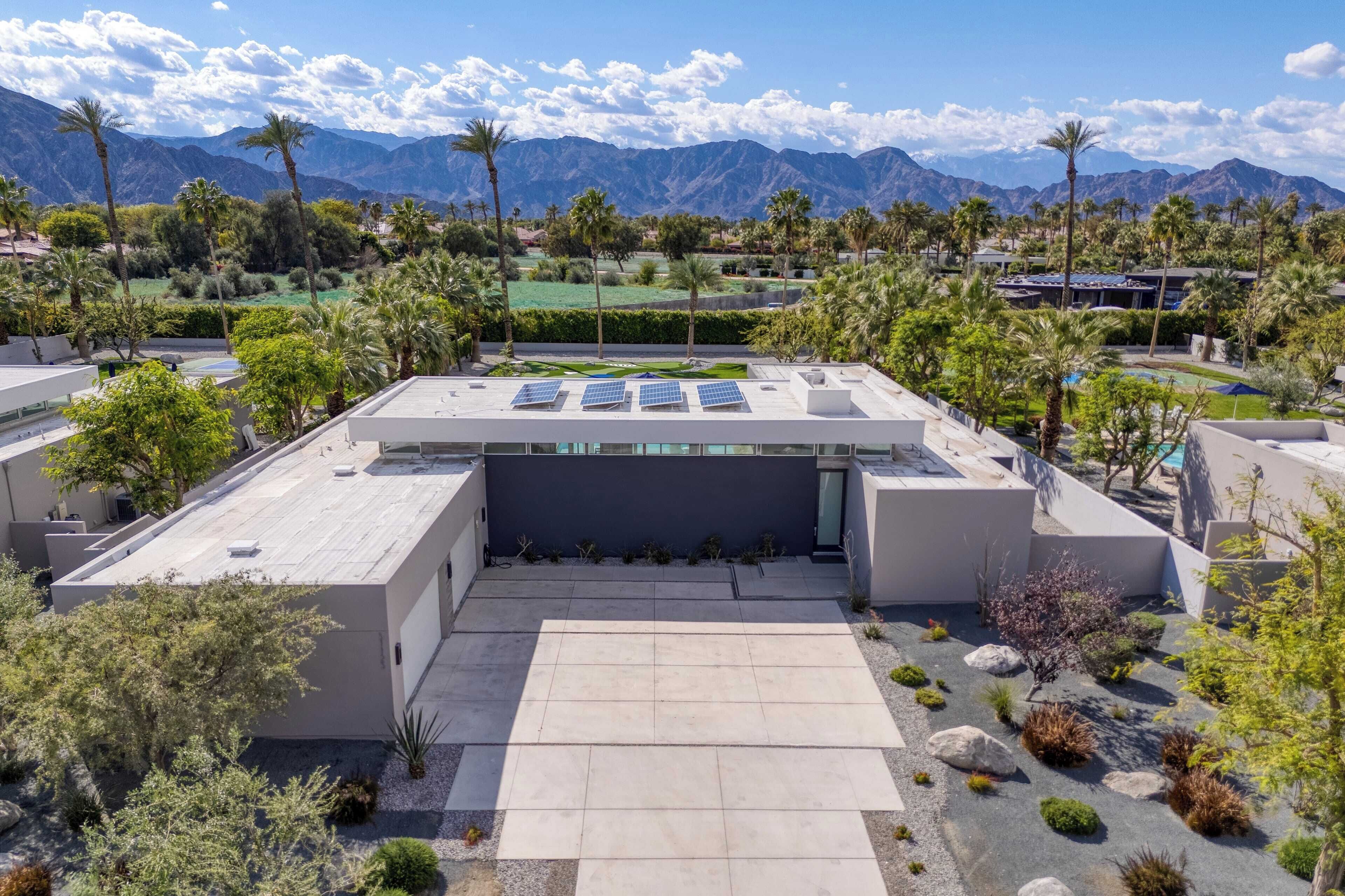 A rooftop terrace with solar panels, surrounded by palm trees and a mountainous backdrop.