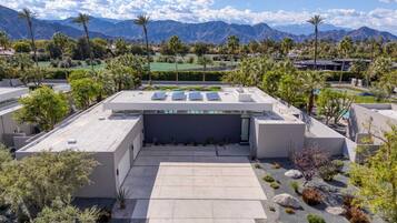 A rooftop terrace with solar panels, surrounded by palm trees and a mountainous backdrop.