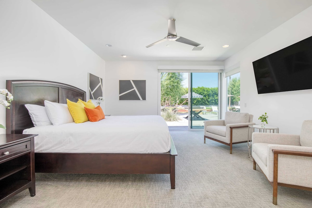 Une chambre moderne avec un grand lit, un ventilateur de plafond, une télévision et une vue sur l’extérieur.
