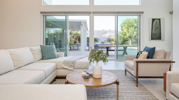 A modern living room with a large sectional sofa, a round coffee table, and a view through glass doors to an outdoor patio. - The Polo Villas by AvantStay (La Quinta)