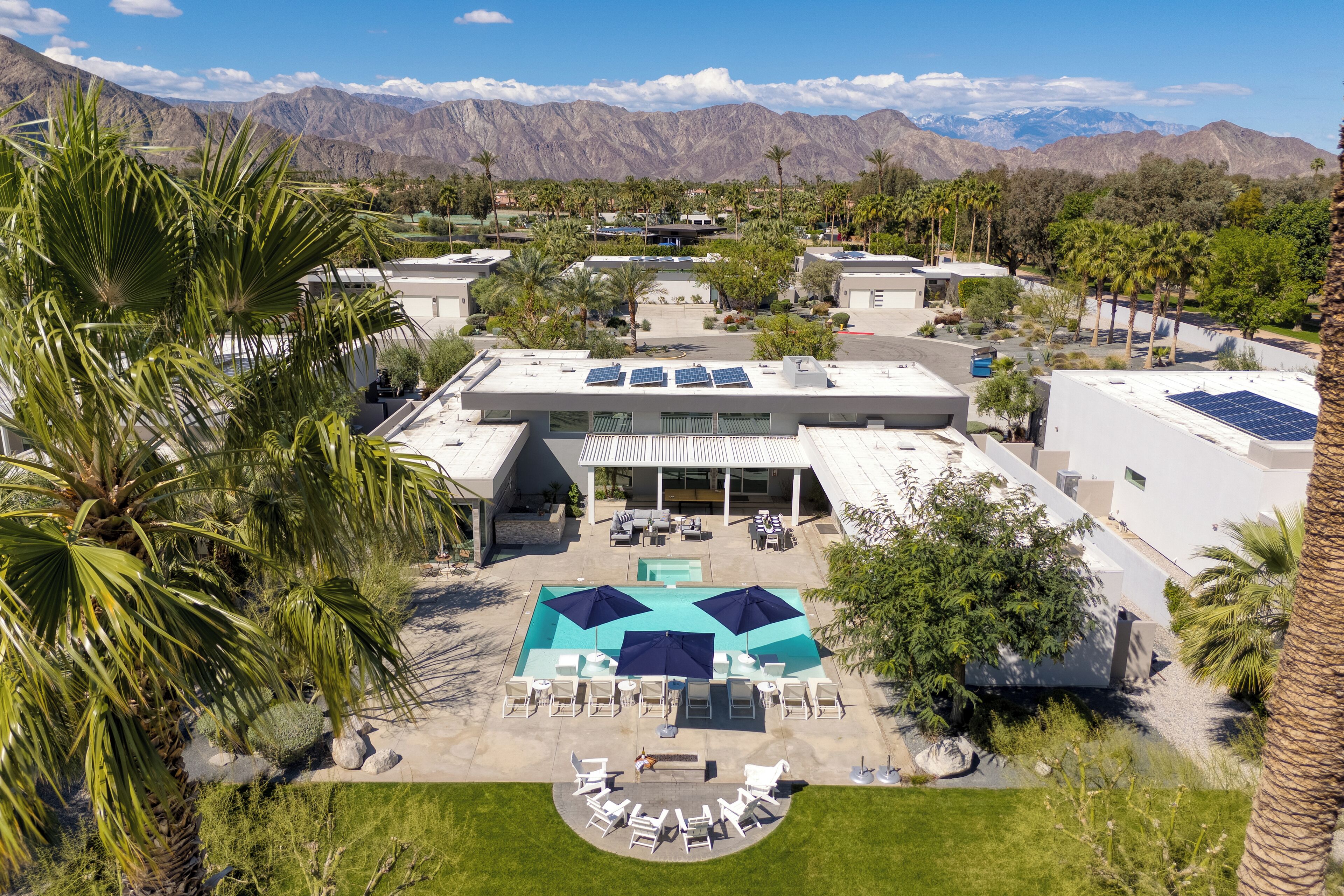 A modern hotel with a rooftop pool, surrounded by palm trees and mountains in the background.