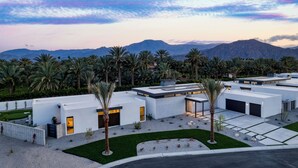 A modern building with multiple garage doors, surrounded by palm trees and a well-maintained lawn. - The Polo Villas by AvantStay (La Quinta)