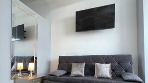 Un dormitorio moderno con un sofá gris oscuro, un espejo grande y un televisor de pantalla plana montado en la pared.