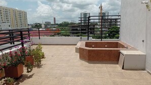 Una terraza en la azotea con jacuzzi, plantas en macetas y vistas a la ciudad.