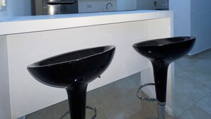 Una cocina moderna con encimera blanca, dos taburetes negros y electrodomésticos de acero inoxidable.