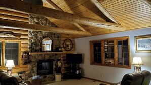 Interior acollidor d'una cabana de fusta amb una llar de pedra, bigues de fusta i sofàs de cuir.