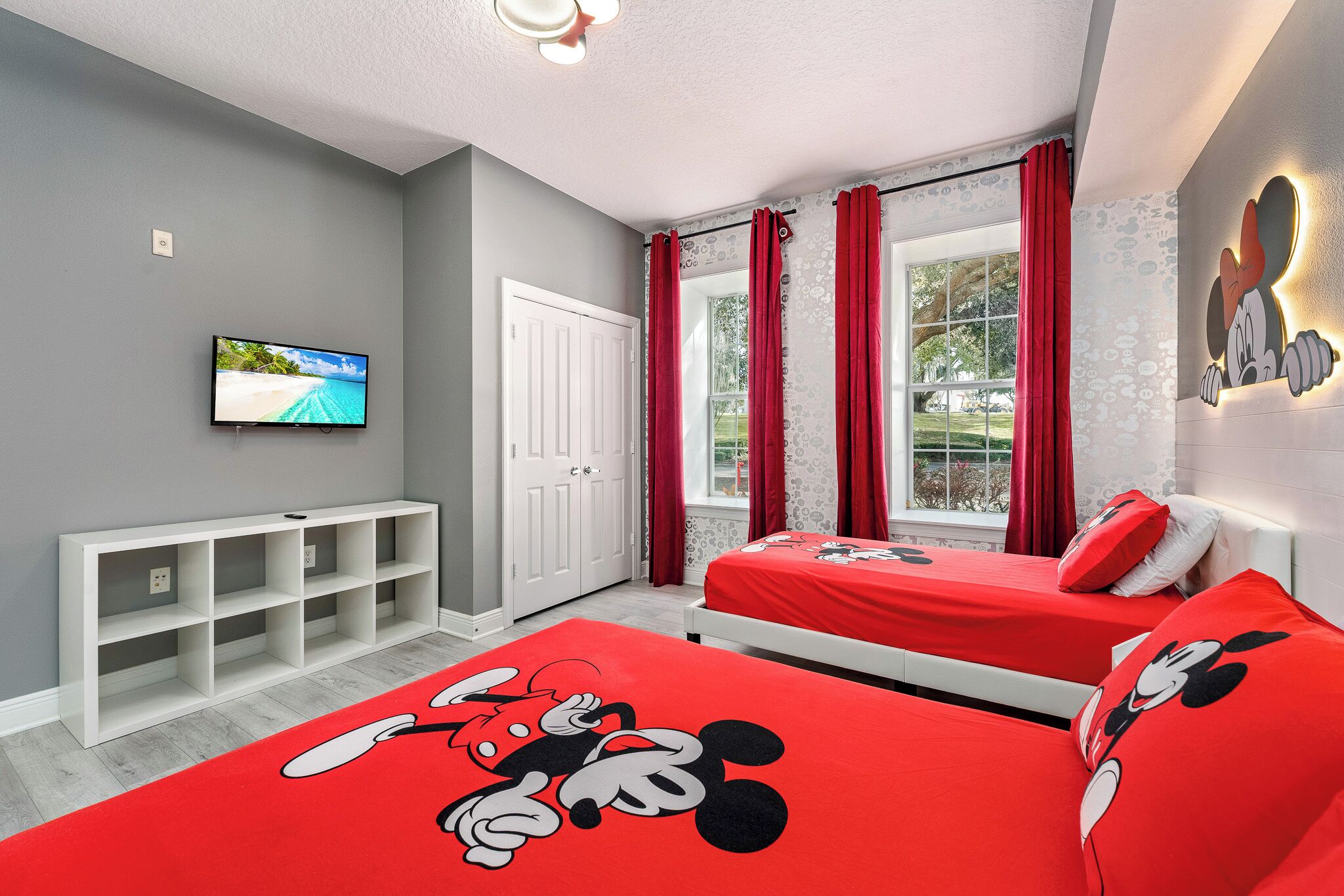 Ein Schlafzimmer mit zwei Betten, einem Fernseher, einer weißen Ablage und einem Fenster mit roten Vorhängen.