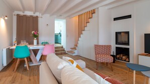 Ein modernes Wohnzimmer mit einer Couch, einem Esstisch mit Stühlen, einer Treppe, einem Kamin und einem Fernseher.