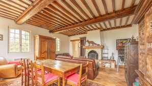 A rustic interior with a wooden dining table, red cushioned chairs, a leather sofa, and a fireplace. - La Renardière - Maison avec vue mer (Barneville-Carteret)